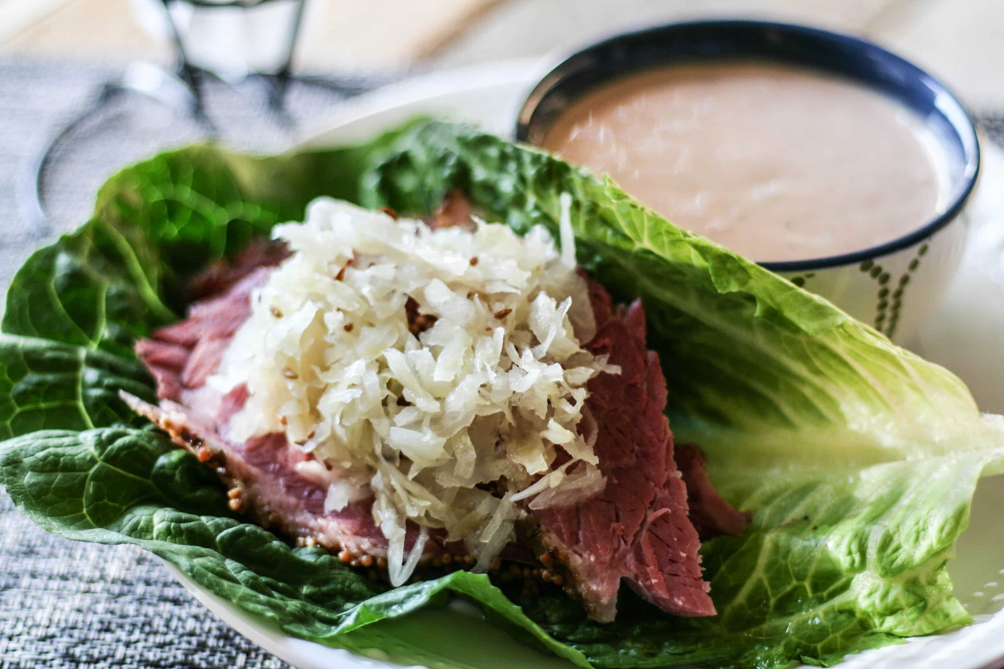 a Paleo Reuben lettuce wrap on a plate with a side of Paleo thousand island dressing